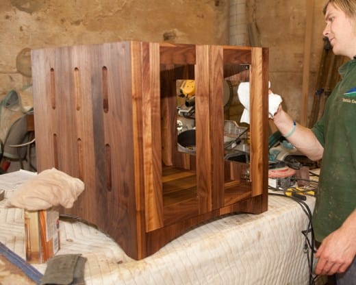 Craftsman hand-finishing a slatted walnut media cabinet on the workshop bench