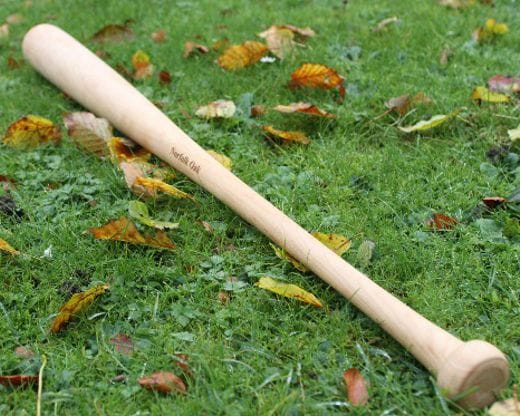 Hand-turned maple baseball bat engraved Norfolk Oak lying on autumn leaves