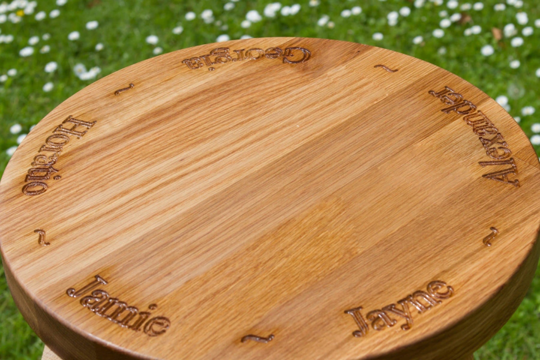 Round oak chopping board engraved with family names around the edge