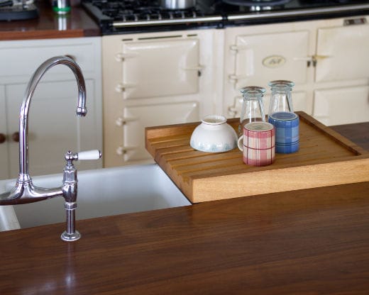 Grooved wooden drainage board holding crockery beside a Belfast sink