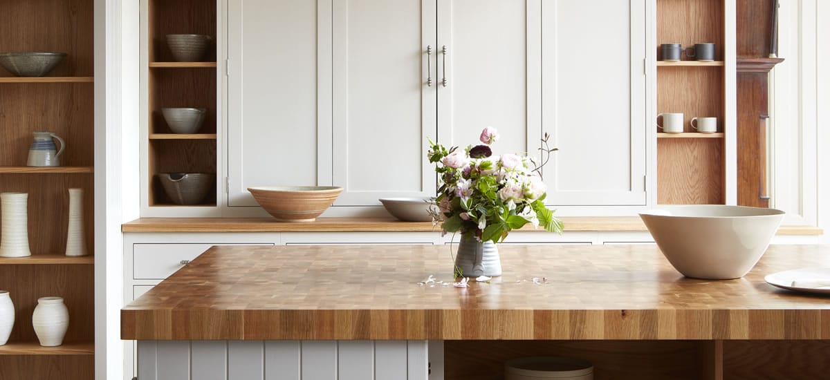 Oak end grain worktop on a kitchen island with cream cabinetry and pottery bowls