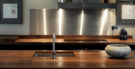 Walnut worktop with inset sink and tap against a brushed steel splashback