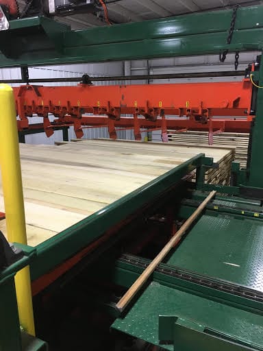 Freshly sawn pale hardwood boards on green sawmill machinery