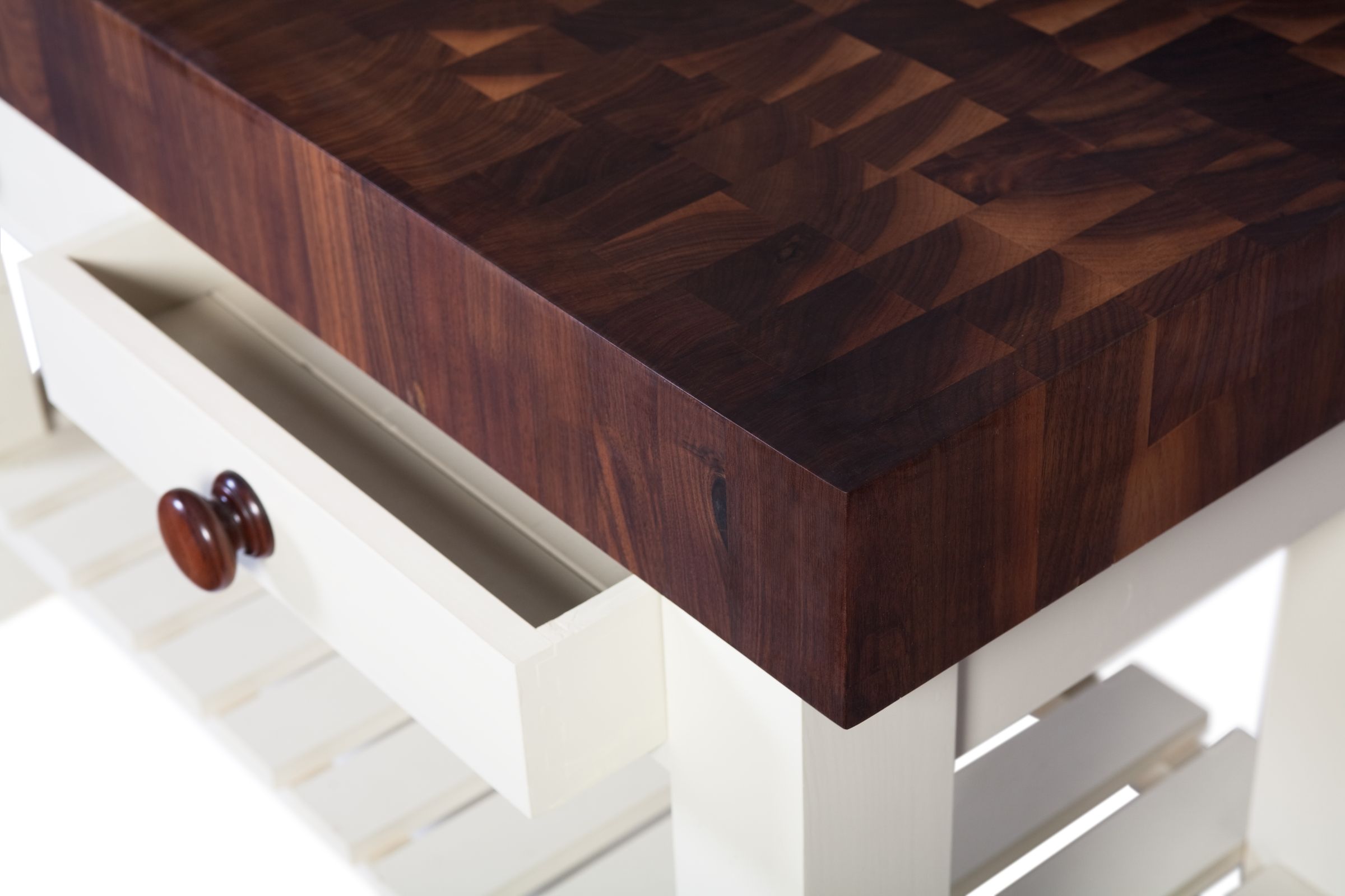 Corner of a thick walnut end grain butcher's block on a cream painted base unit
