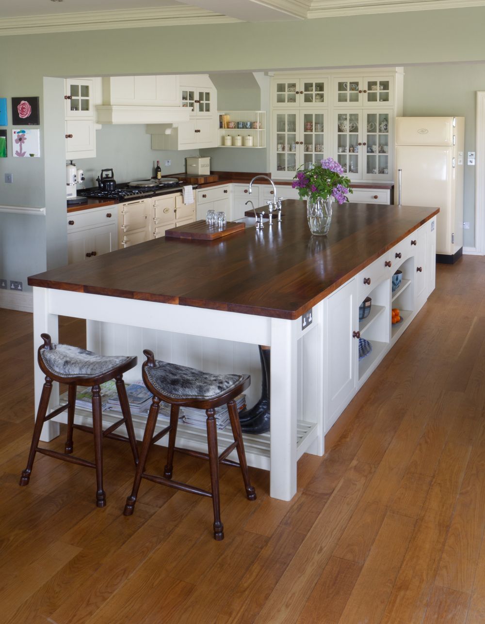 Large white kitchen island with dark walnut top, saddle stools and cream Aga behind