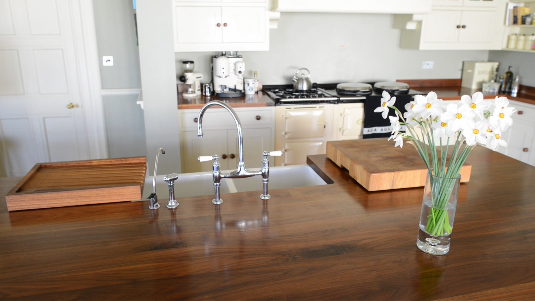 light-kitchen Dark walnut island worktop with chrome bridge tap, white narcissi and a cream Aga behind