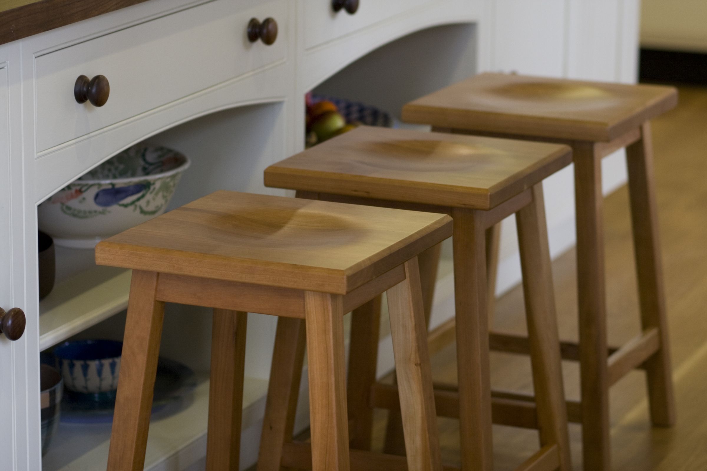 oak kitchen stools Three oak kitchen stools with scooped seats lined up along a white dresser