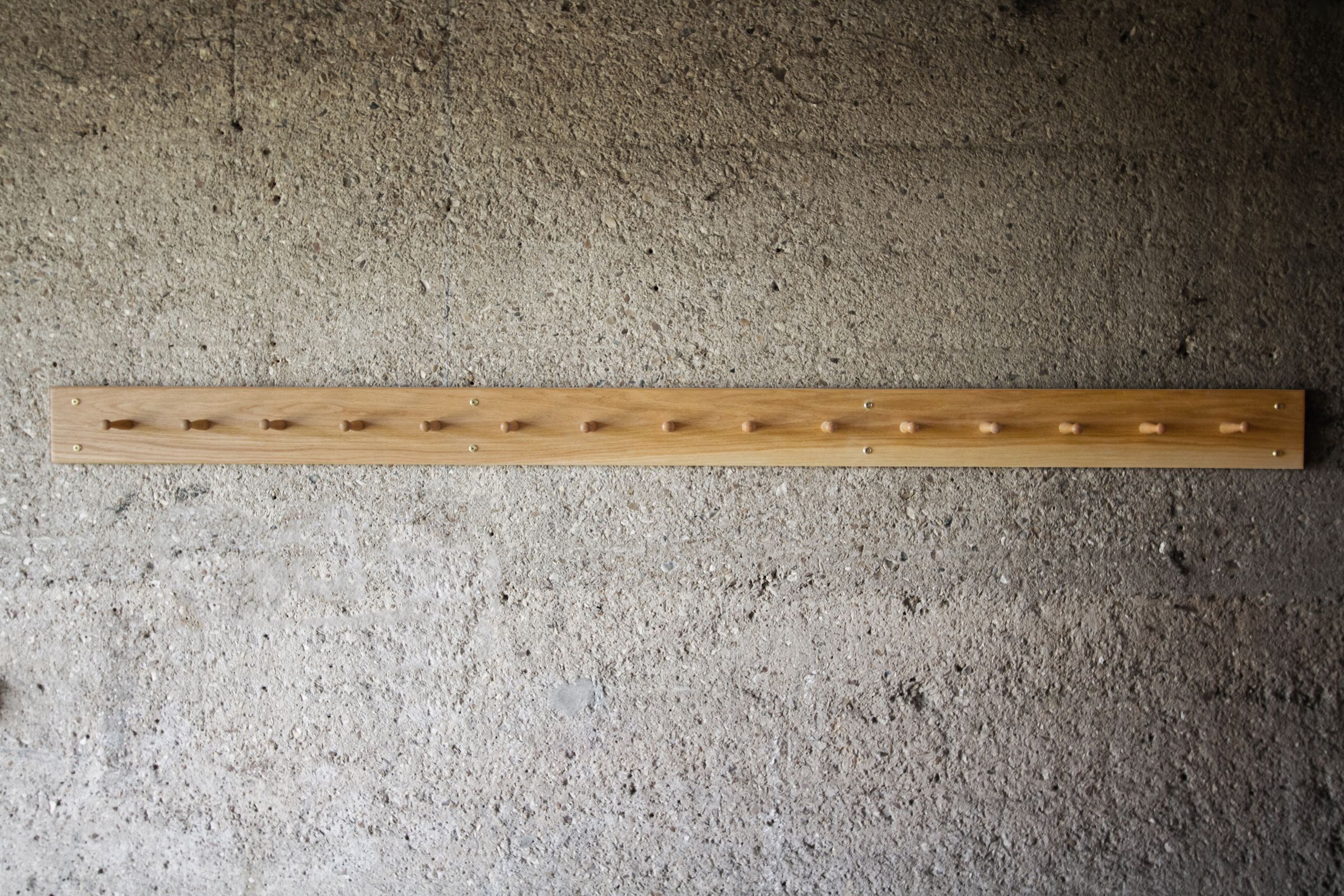 long oak shaker peg rail Extra-long oak Shaker peg rail with fifteen pegs mounted on a concrete wall
