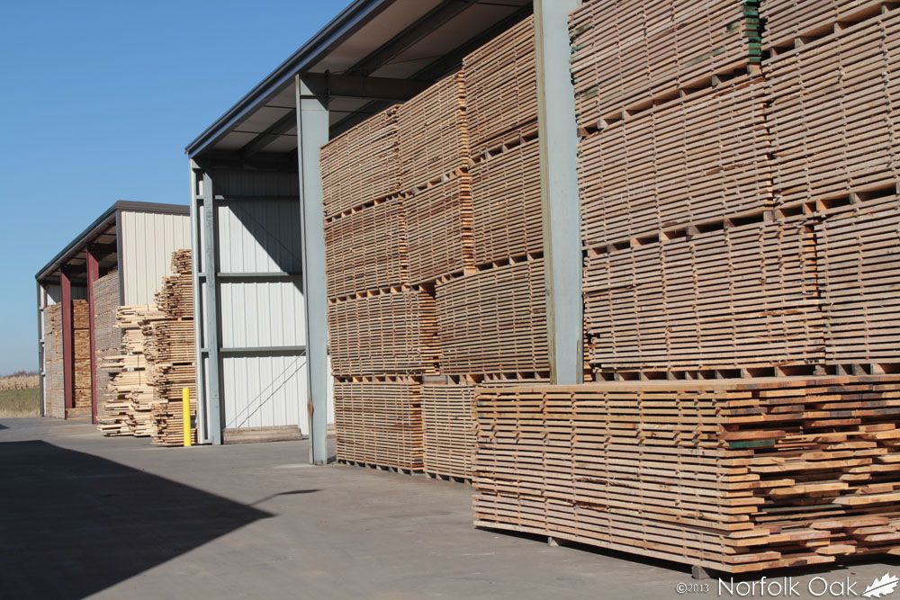 Tall stacks of sawn boards air drying in stickered piles outside a timber shed