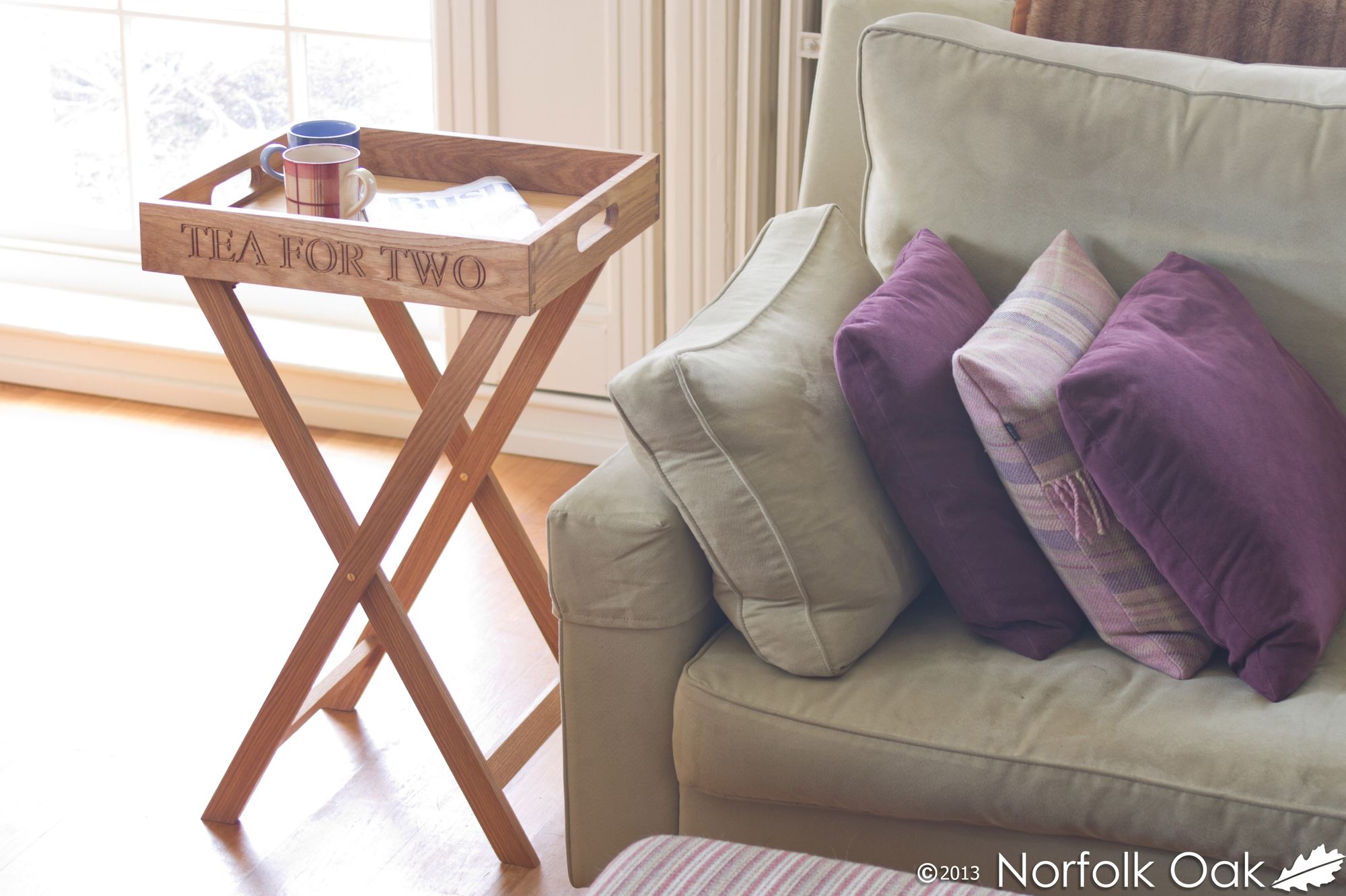 Wooden butler's tray engraved Tea For Two beside a sofa with purple cushions