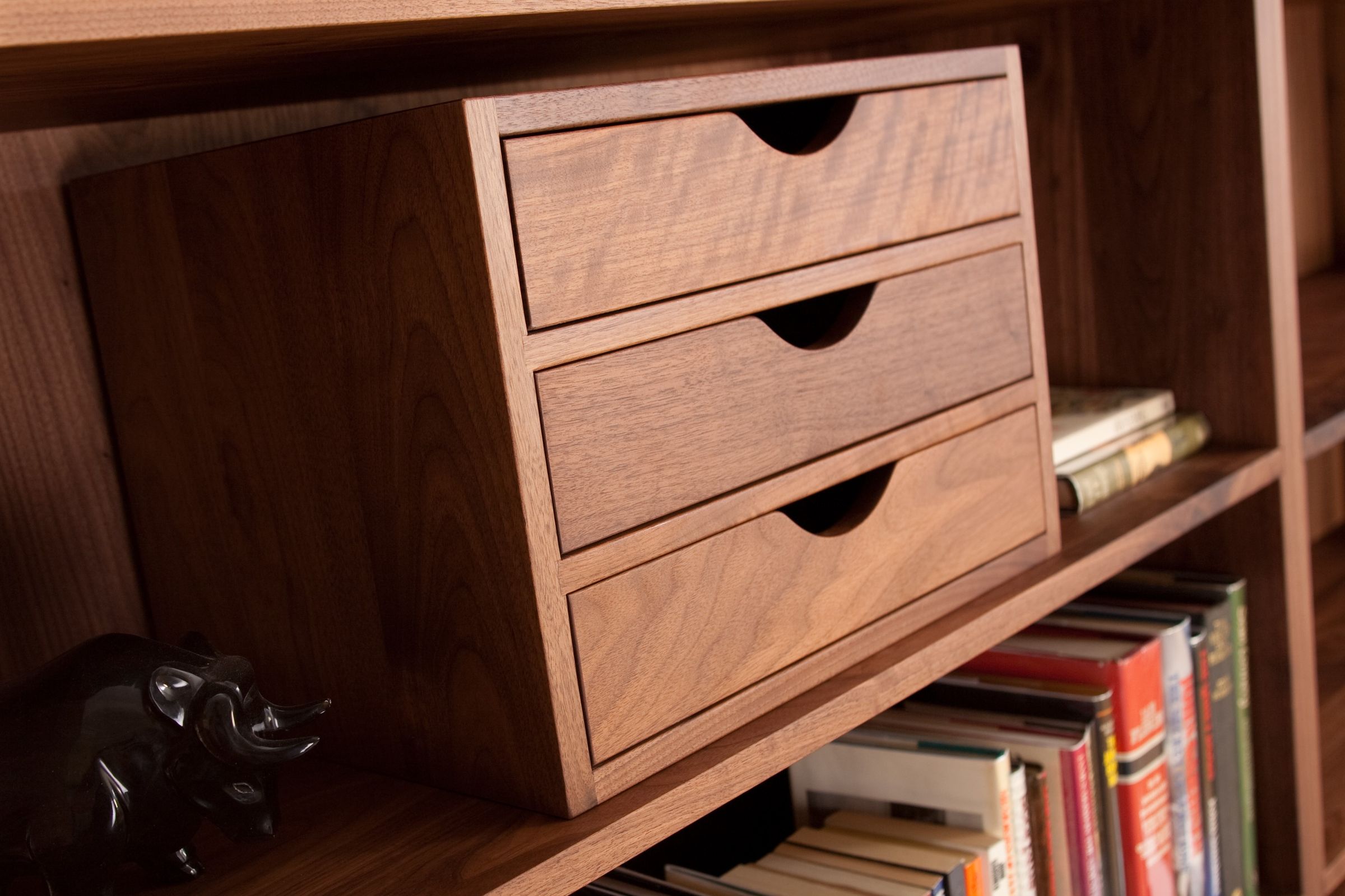 Three-drawer walnut filing box sitting on a bookshelf beside rows of books