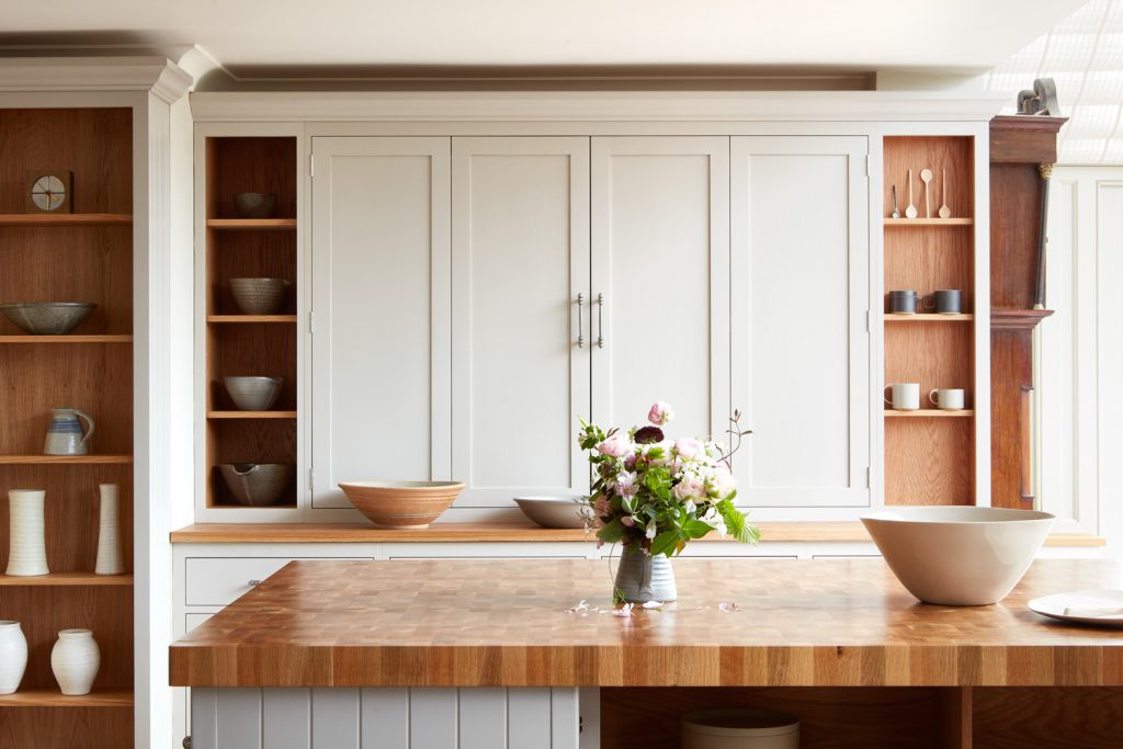 End grain butcher's block island with fresh flowers, cream cabinetry and oak shelving