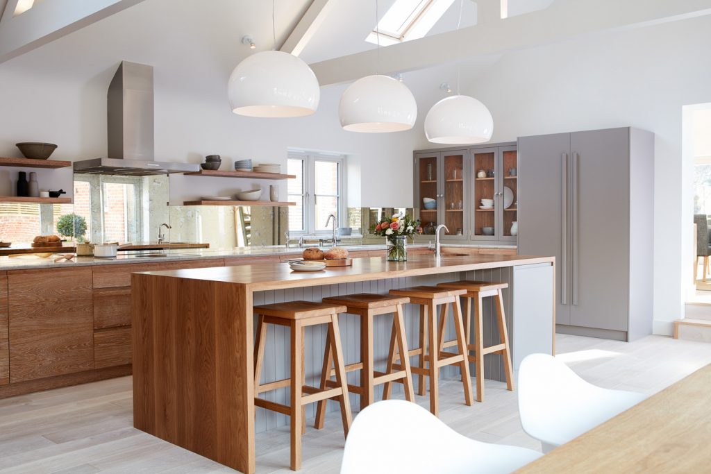 Bright open-plan kitchen with oak island, wooden bar stools and white pendant lights