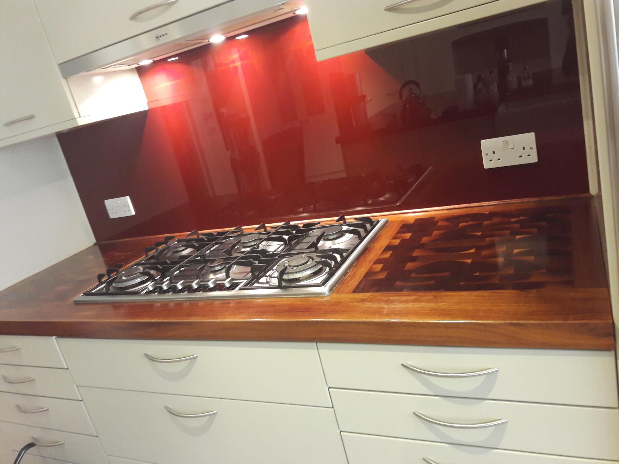 Gas hob set into a wooden worktop with end grain insert, beneath a red glass splashback